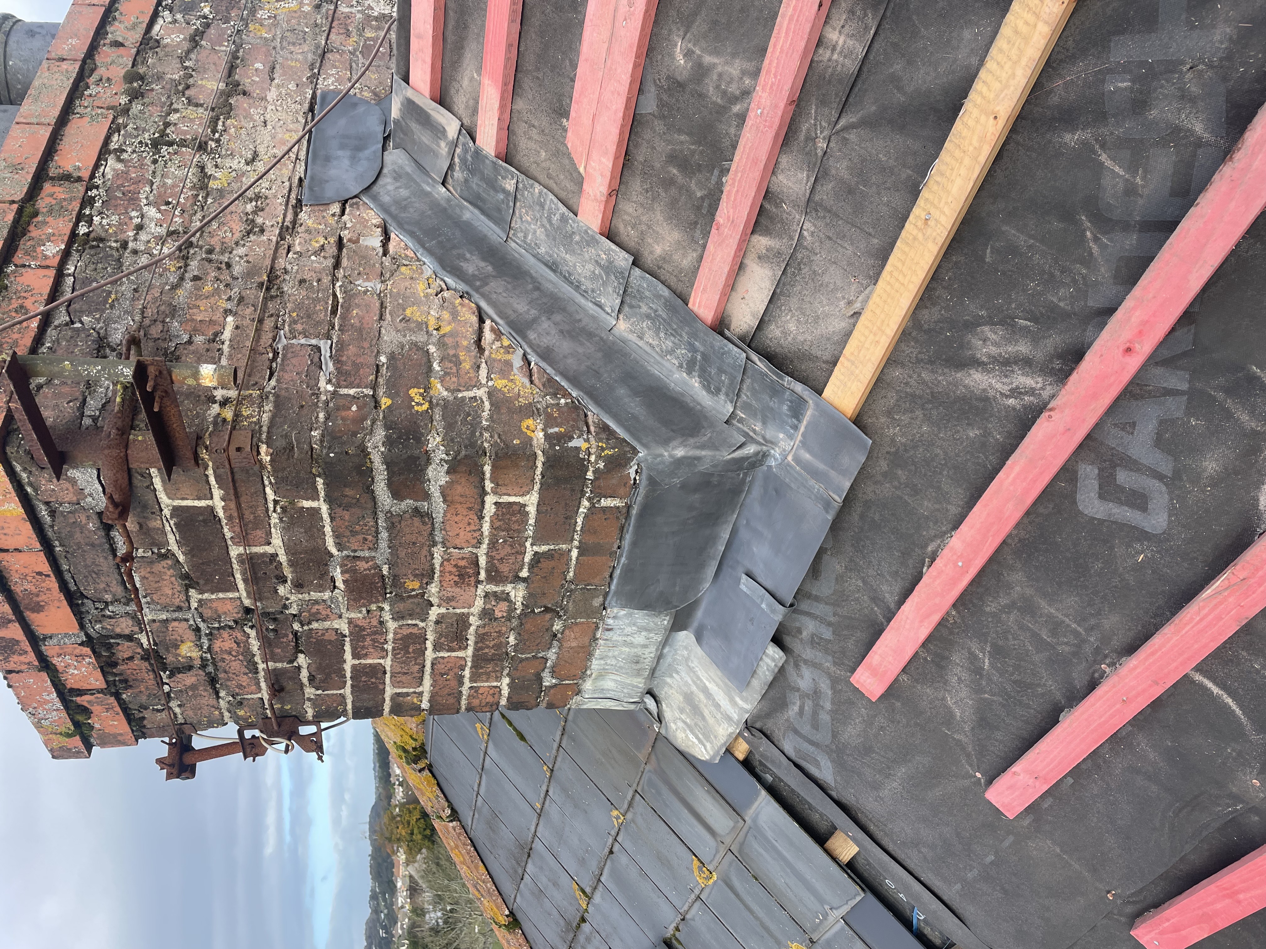Bespoke Code 4 stepped lead flashing chased into a heritage brick chimney stack. Expert maritime weatherproofing and leadwork fabrication by Raven Roofing Services in Torquay.
