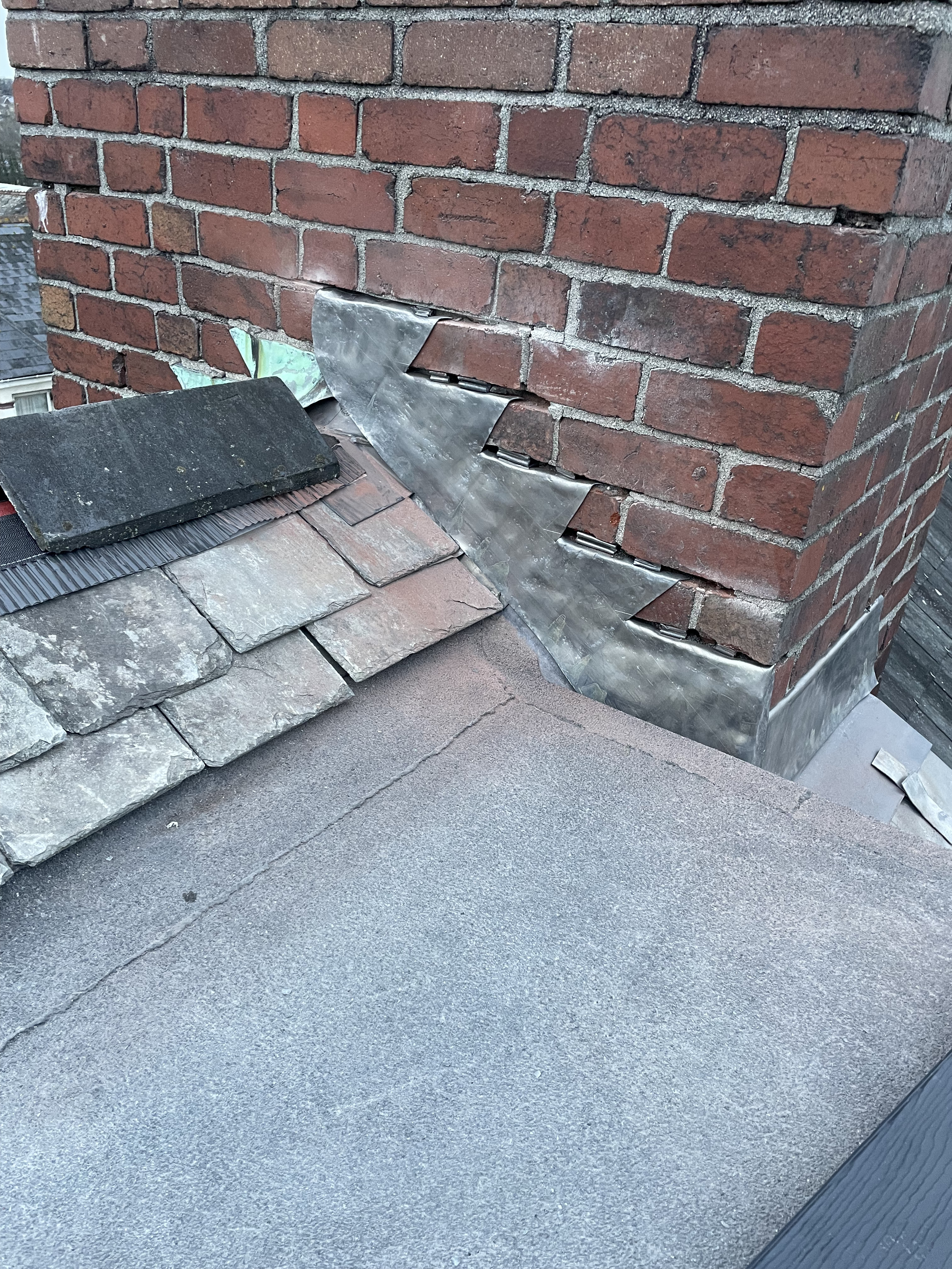 Intricate stepped lead flashing installation on a heritage brick chimney in Totnes TQ9, overlapping reclaimed Delabole slates to provide a permanent watertight seal against Devon coastal weather.