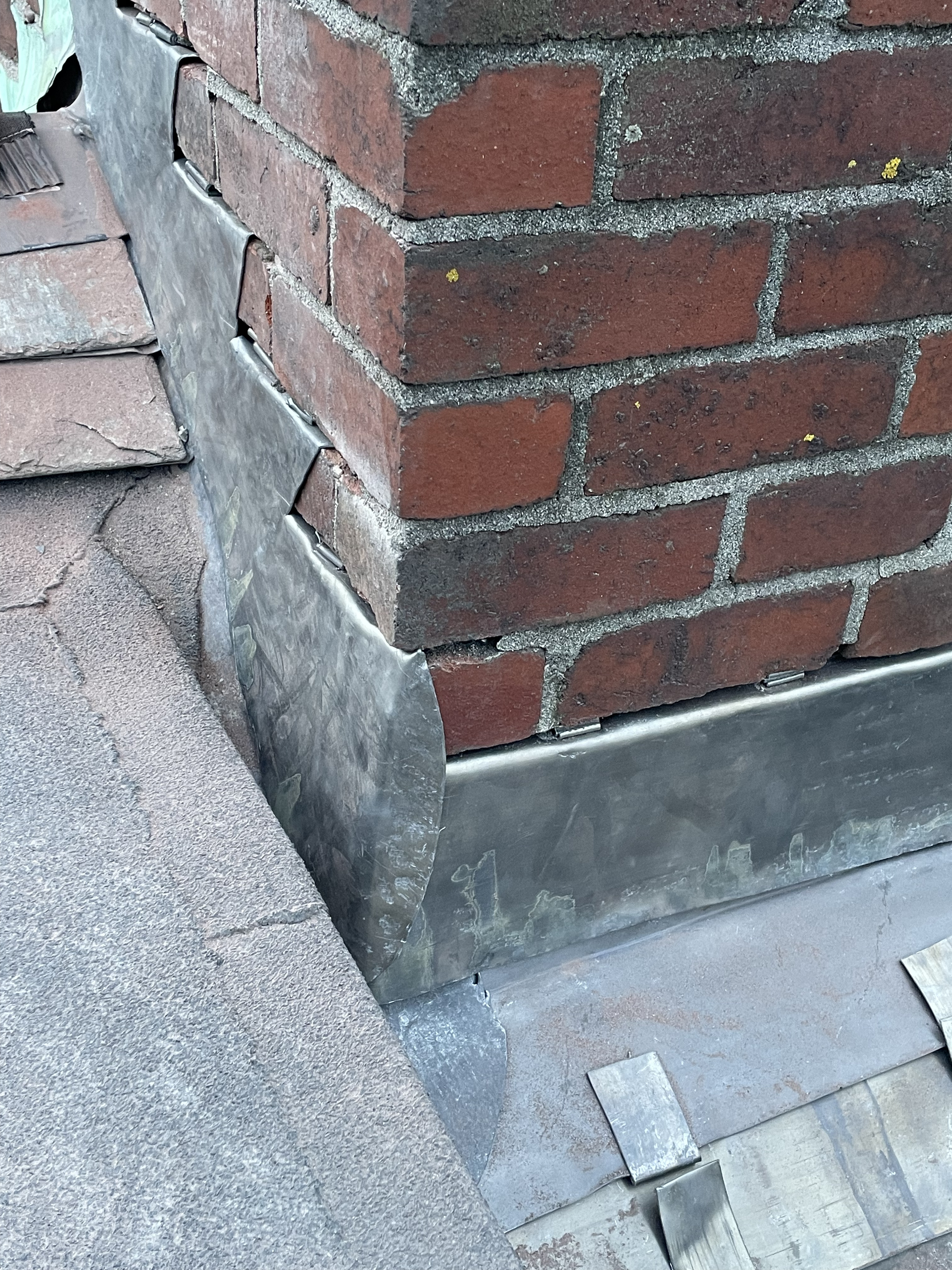 Detailed corner view of bespoke stepped leadwork and front apron flashing on a masonry chimney stack in Totnes, marrying traditional brickwork with reclaimed Delabole slates.