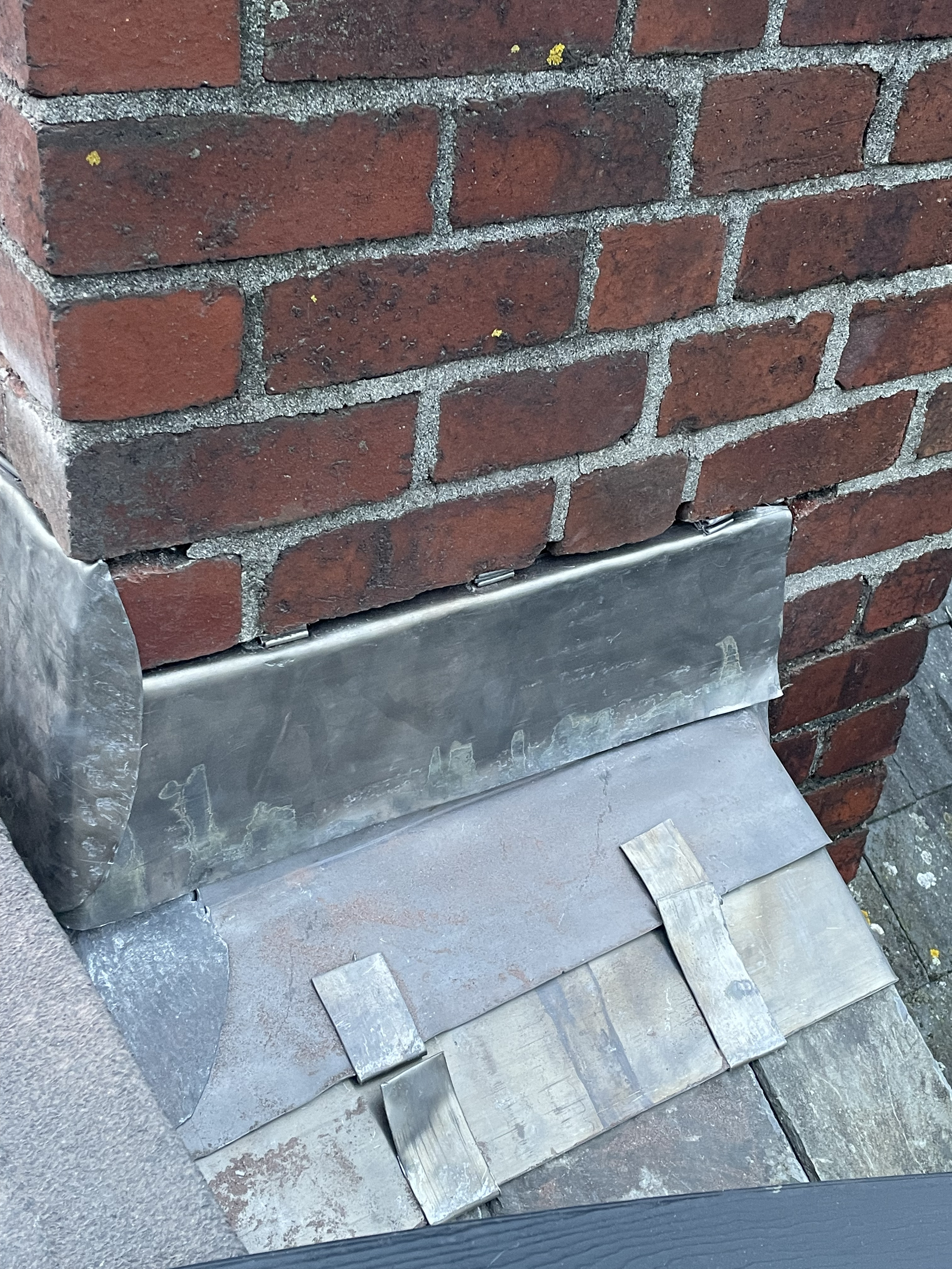 Close-up of premium Code 4 stepped lead flashing chased into a traditional brick chimney stack on a Totnes roofing project, ensuring BS 5534 compliant waterproofing.