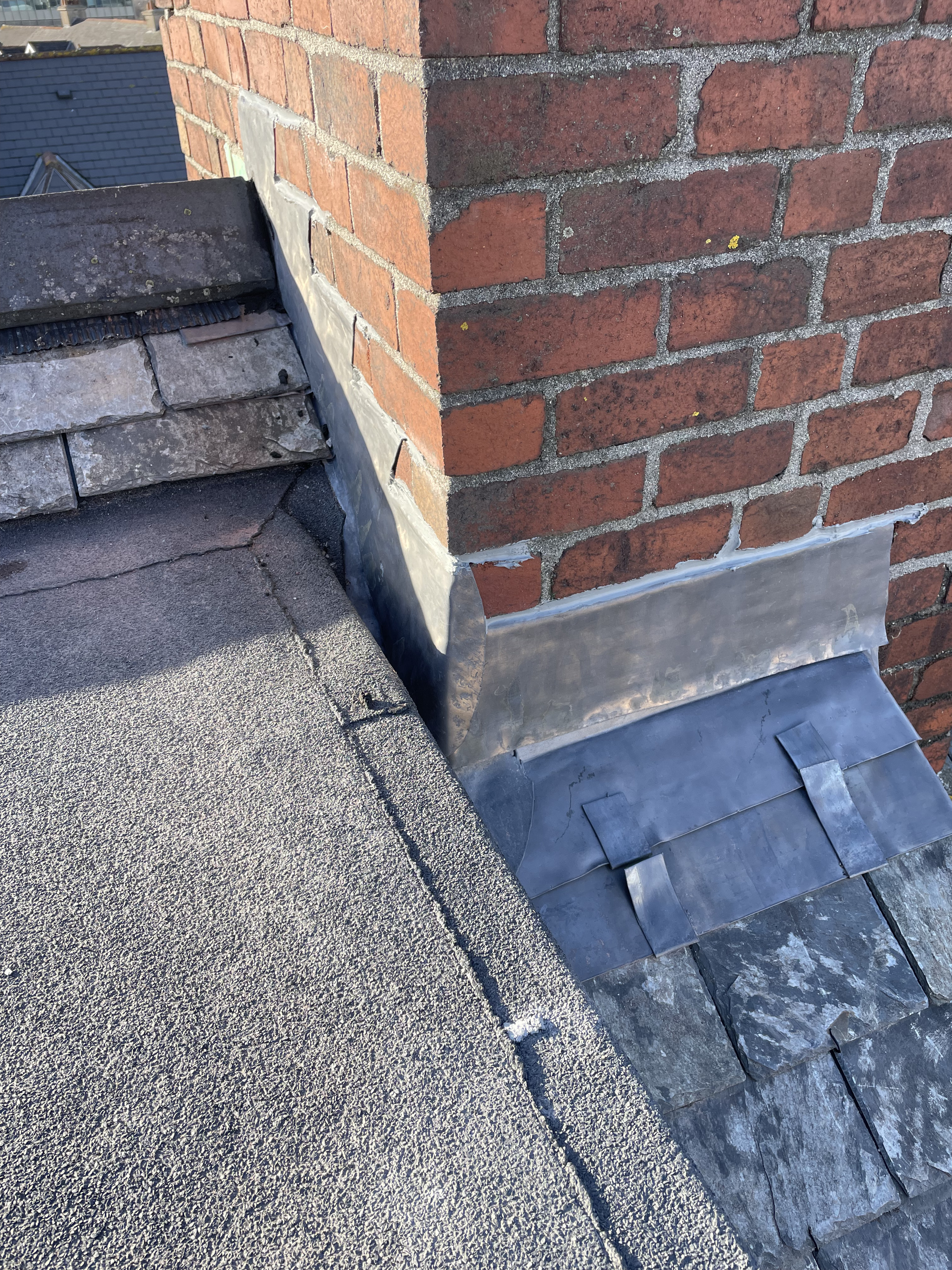 Expert chimney leadwork in Totnes, Devon, featuring stepped flashings and lead apron integrating a brick chimney stack with an SBS flat roof and reclaimed Delabole slate.