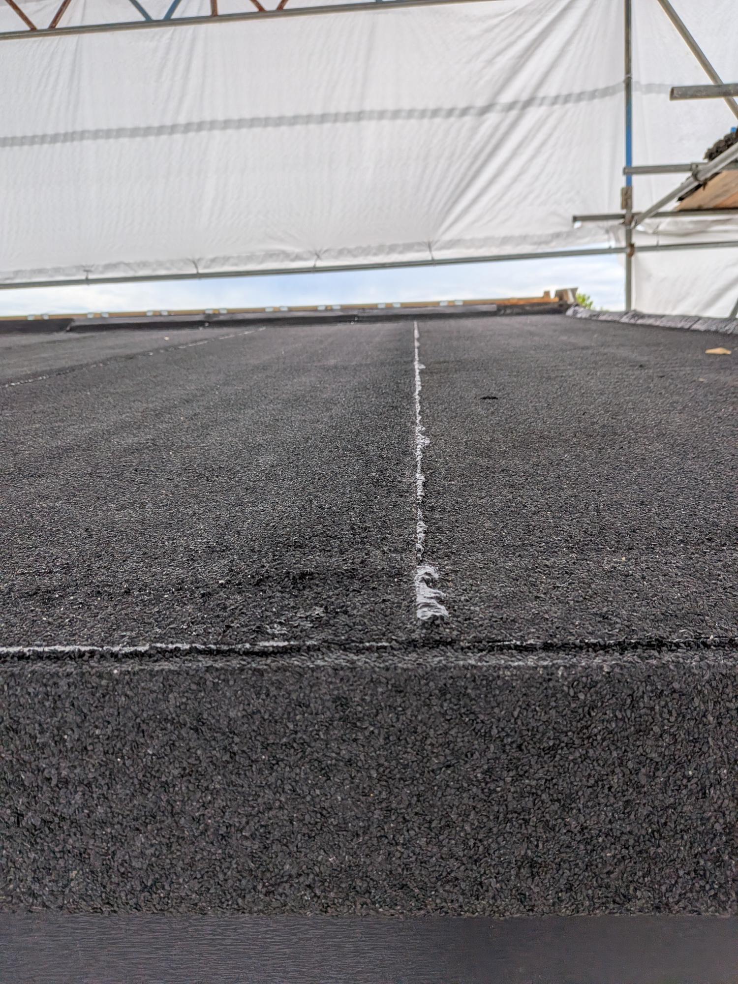 Close-up detailing of a fully bonded SBS mineral cap sheet seam during a flat roof rebuild in Devon