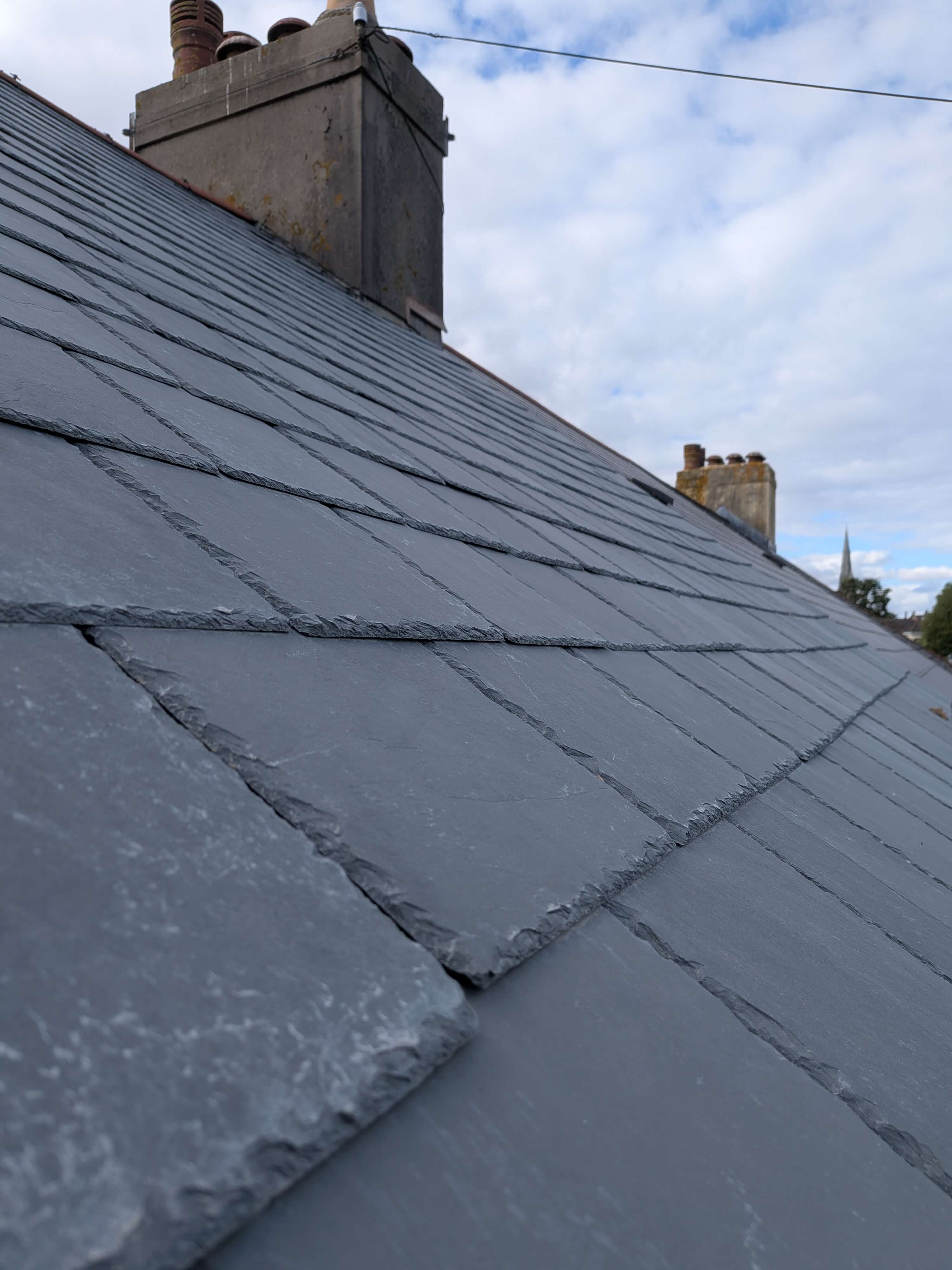 Close-up of newly installed Brazilian slate tiles and chimney leadwork in Torbay, demonstrating precision cutting and maritime weatherproofing.