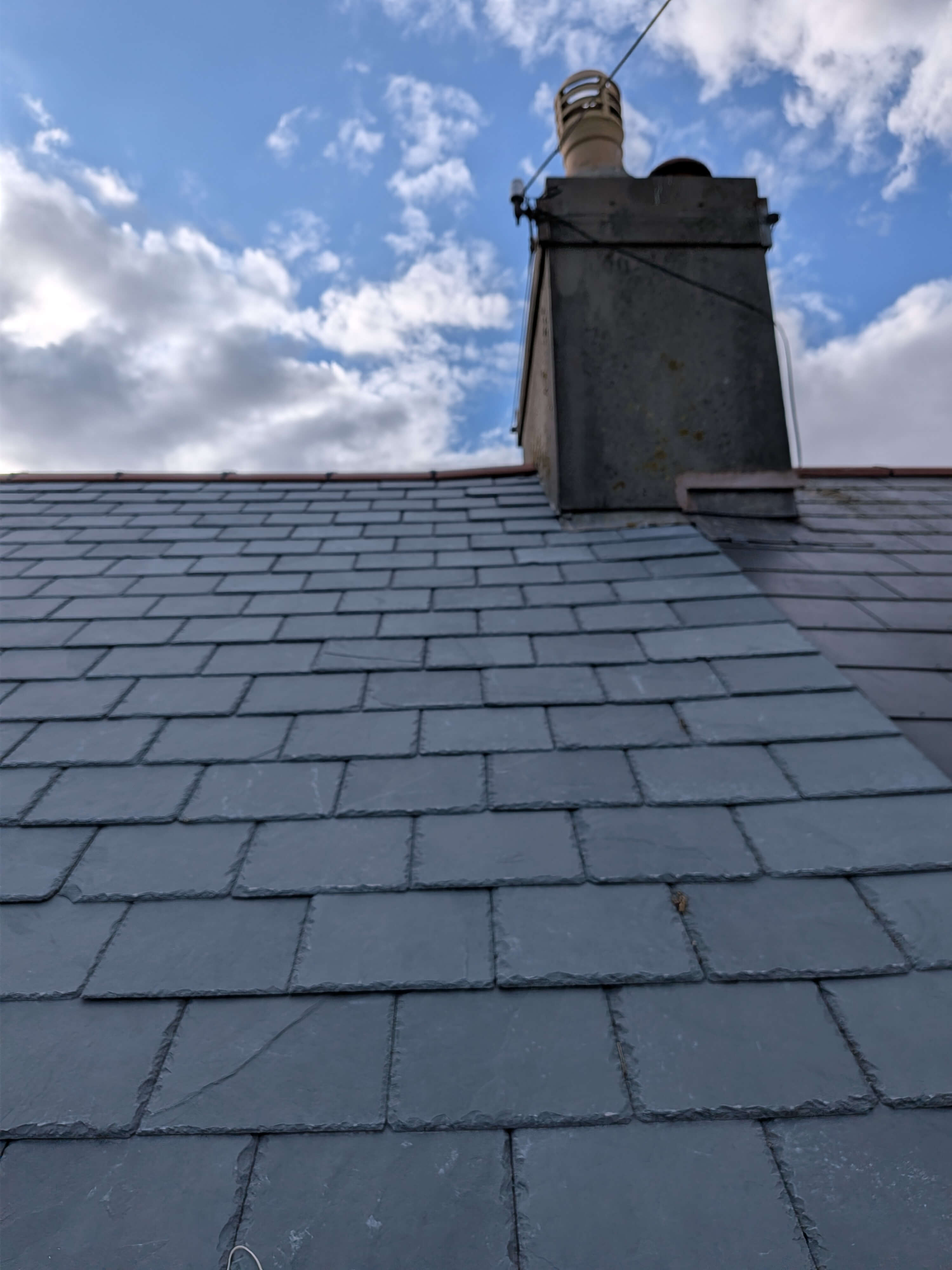Finished Brazilian slate roof integration with existing chimney stack structure in Torbay TQ3, featuring permanent leak resolution and renewed aesthetic value.